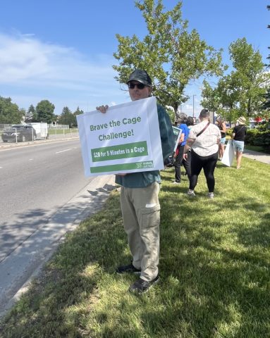 Supporter with sign: Brave the Cage Challenge! $20 for 5 Minutes in a Cage