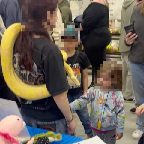 A person with a large yellow snake draped over their shoulders talking to young children at an event.